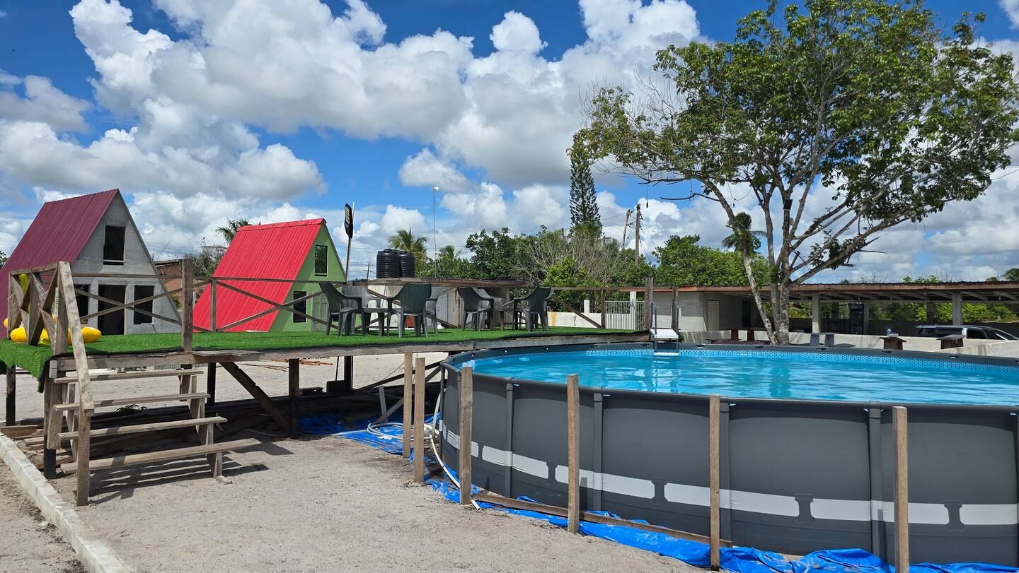 Above-ground pool with a turf deck and cabins behind